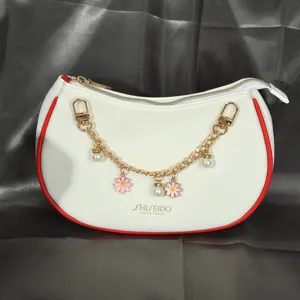Détail d'un sac à main blanc avec une chaîne décorative en fleurs dorées et perles