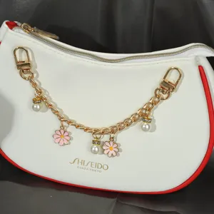 Vue rapprochée d'une élégante chaîne de sac dorée avec breloques fleurs roses et perles fines