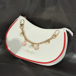 Gros plan d'une chaîne décorative dorée pour sac avec breloques fleurs roses et perles