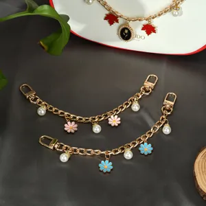 Détail de breloques de sac en métal doré avec fleurs en émail et perles blanches
