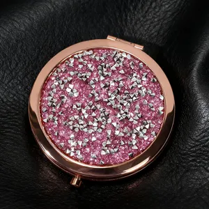 Close-up of a rose gold folding compact mirror with pink glitter and silver studs.
