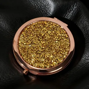 Close-up of a golden glitter round folding makeup mirror with studs on black leather.