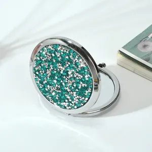 Detailed view of round metal folding makeup mirror with sparkling green rhinestones