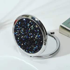 A detailed view of a round folding makeup mirror with a black diamond glitter lid.