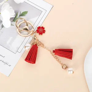 Detail of a cute red tassel keychain with flower charm and pearls for bag decor.