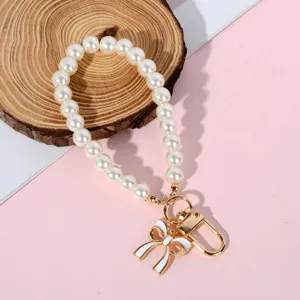 Elegant white pearl phone charm featuring a gold bow pendant and clasp on pink background