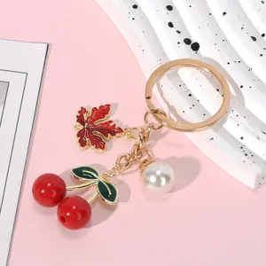 Charming gold-tone keychain featuring red resin cherries, maple leaf charm and a white pearl