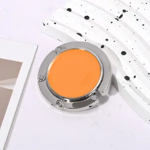 Detailweergave van een draagbare, opvouwbare metalen tassenhaak in zilver en oranje.