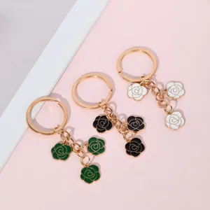 Close-up detail of three rose flower enamel keychains in green, black, and white colors