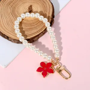 Detail of pearl phone strap featuring a red flower charm and golden lobster clasp.
