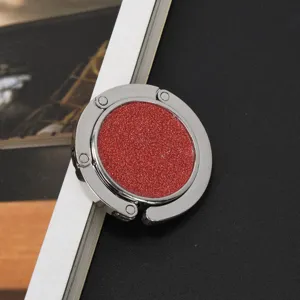 Detailaufnahme eines runden, faltbaren Handtaschenhalters mit rotem Glitzer-Finish