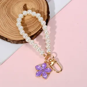 Close-up of pearl phone chain with purple flower charm and golden clasp on wood background