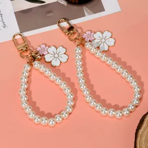 Close-up detail of elegant white pearl phone wristlet with delicate floral charms