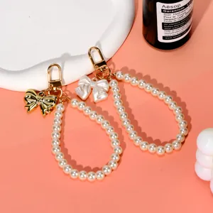 Detailed view of pearl beaded wrist strap with elegant gold and white bow charms