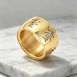 Gros plan détaillé d'une large bague dorée avec des silhouettes ajourées et des strass étincelants.