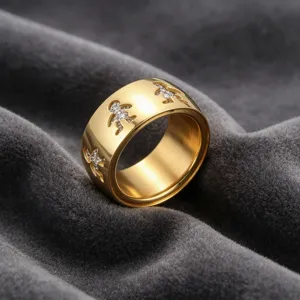 Vue détaillée d'une large bague dorée ajourée avec des motifs de petits personnages.
