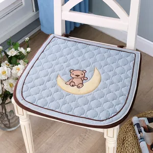 Gros plan détaillé du coussin de chaise matelassé bleu avec un mignon ours brodé sur la lune.