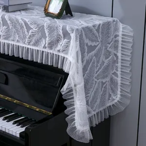 Gros plan sur la housse de piano en dentelle blanche avec motif de feuilles et franges.