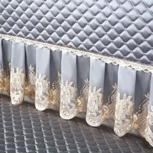 Detailed shot of quilted grey sofa cover featuring elegant lace floral embroidered skirt trim.