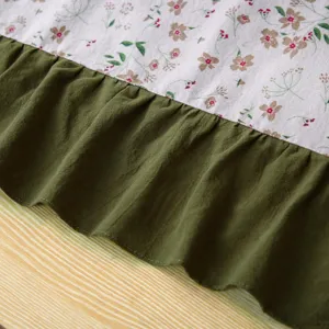 Dettaglio ravvicinato di un grembiule in tela floreale con orlo volant verde oliva.