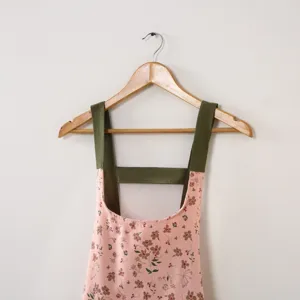 Dettaglio grembiule floreale, tessuto rosa con motivo floreale marrone e cinghie.