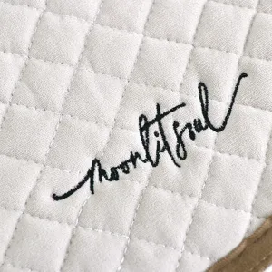 Close-up detail of beige quilted dining chair cushion featuring elegant embroidered lettering design.