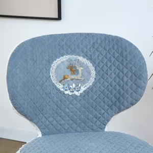 Dettaglio coprisedia trapuntato blu, elegante motivo ricamato con cervo e pizzo per sedia da pranzo.