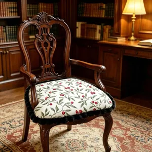 Detail view of the vintage wooden armchair featuring a botanical print cushion with black fringe.