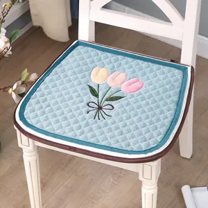 Detail shot of blue quilted chair cushion featuring 3D embroidered tulip flowers and border.