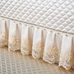 Quilted sofa cover detail showcasing delicate embroidered lace ruffle trim, elegant decor.