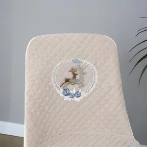 Detail view of quilted beige chair cover featuring delicate embroidered deer and floral lace wreath.