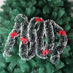 Detailed view of dark green Christmas tinsel garland with white tips and red bows.
