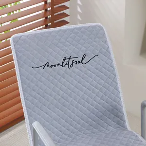 Détail de coussin de chaise matelassé gris, tissu doux avec broderie élégante et bord blanc.