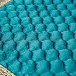 Primer plano de detalle de cojín de silla acolchado de terciopelo verde azulado con borde.
