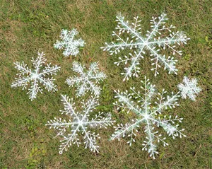 Detailed view of various sized white plastic Christmas snowflake ornaments on green grass