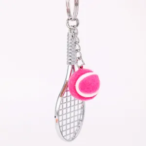 Detalle de un llavero con una mini raqueta de tenis plateada y pelota de tenis rosa.
