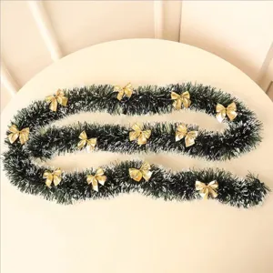 Close-up detail of dark green Christmas tinsel garland with white tips and golden bows.