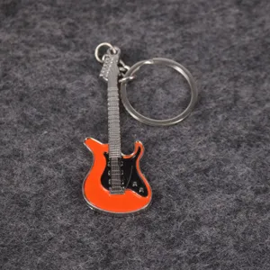 Vista detallada de un llavero con forma de guitarra eléctrica naranja sobre fondo gris