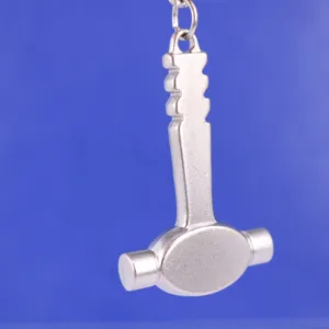 Detalle de cerca de un llavero con forma de martillo de metal plateado sobre fondo azul.