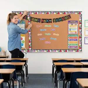 Teacher applying colorful school supply themed bulletin board border in a bright classroom.