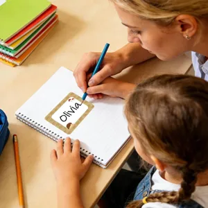 Young girl writing on a self-adhesive name sticker with hedgehog pattern on a notebook