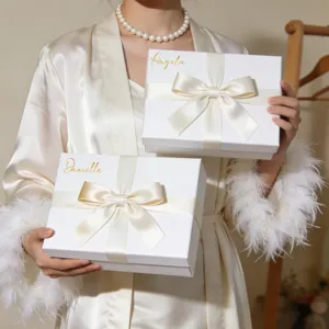 Detailansicht von goldenen Vinyl-Namensaufklebern auf weißen Geschenkboxen mit Crèmeschleifen