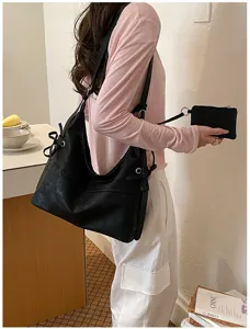 Vista lateral de un bolso hobo de cuero suave negro con un pequeño estuche a juego.