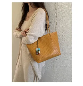 Detalle de un bolso tote tejido en color amarillo mostaza con un dije de colores en una modelo