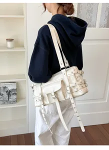 Close-up detail of a creamy-white soft leather tote bag with punk buckle straps and grommets
