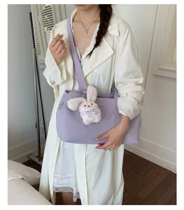 Lifestyle detail of a purple nylon tote bag with a cute white bunny plush charm accessory.