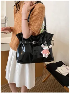 Gros plan du sac cabas noir brillant avec boucle décorative et porte-clés chien en peluche.