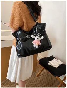 Détail d'un sac cabas en cuir verni noir avec un adorable porte-clés chien porté par un mannequin