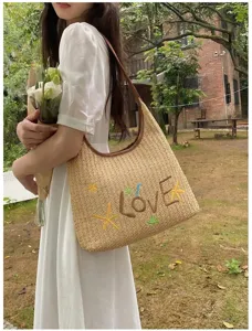 Vista dettagliata di una borsa tote in paglia intrecciata con ricamo LOVE indossata da una modella