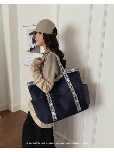 Große marineblaue Strandtasche aus Netzstoff mit Buchstabengurten am Modell getragen